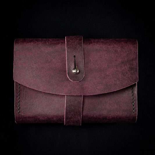 The Shroud handmade leather tarot deck case in Prugna, the Cosmic colourway, photographed flat from the front with its wrap strap fastened over the collar button