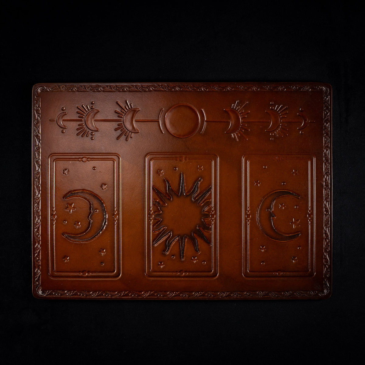 The Astro leather tarot mat seen from above, with a sun between two crescent moons and a band of moon phases across the top
