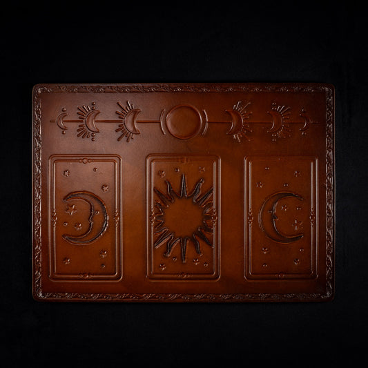 The Astro leather tarot mat seen from above, with a sun between two crescent moons and a band of moon phases across the top