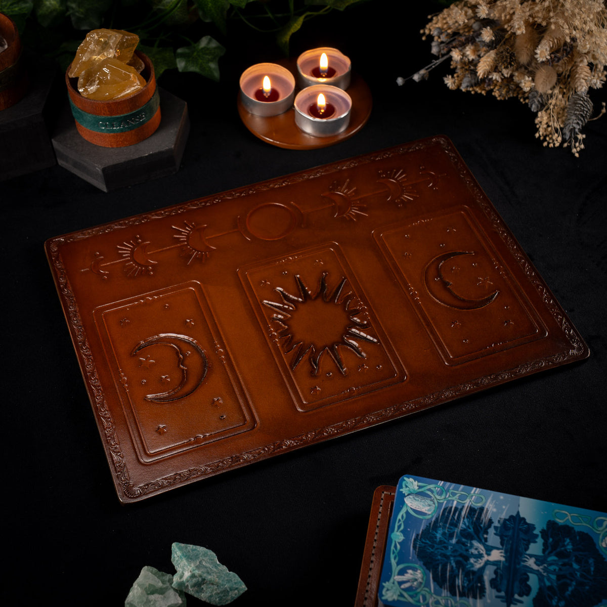 The Astro leather tarot mat with its three card placements empty, a tarot deck resting beside it among candles and crystals