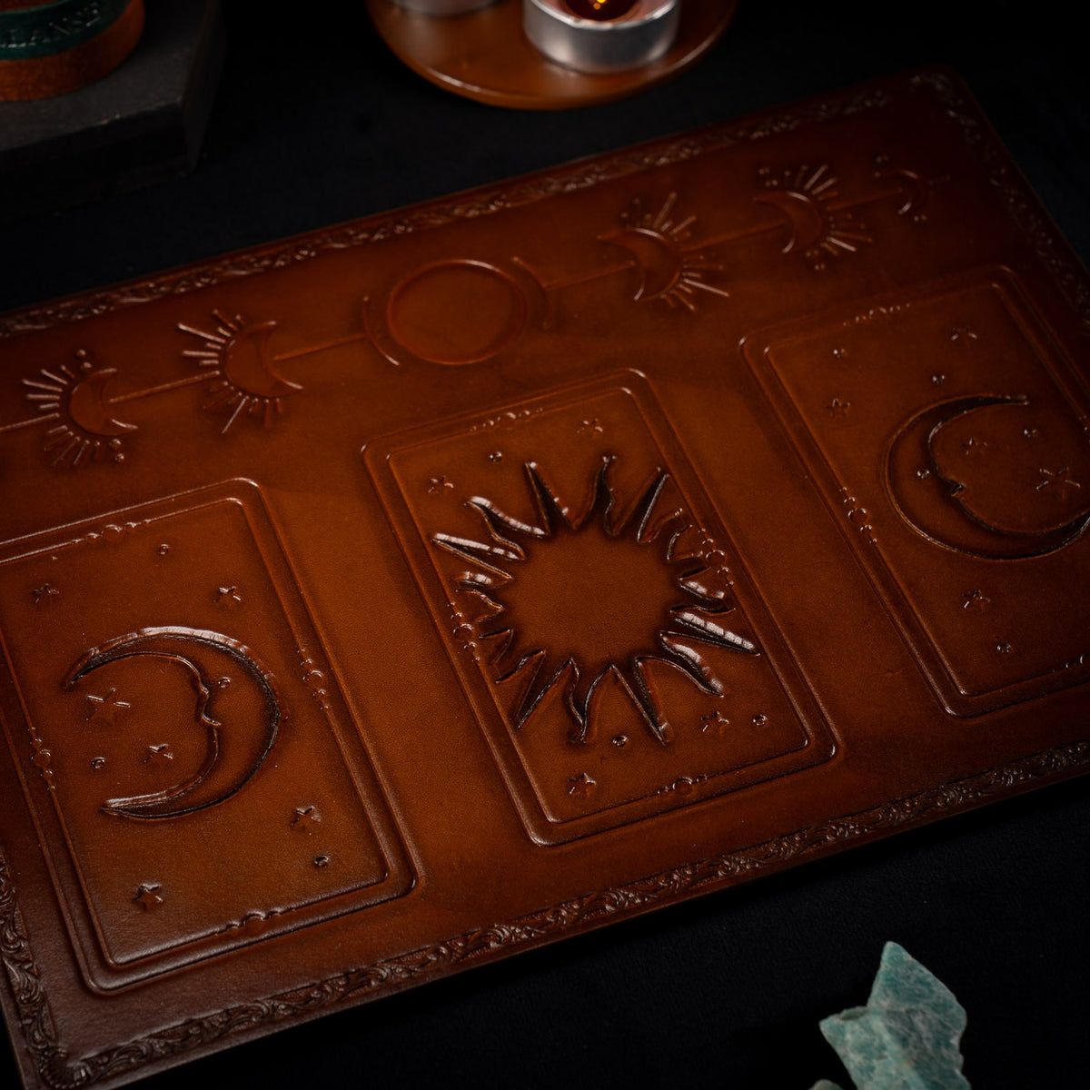 Angled view of The Astro leather tarot mat showing the three card placements, a crescent moon either side of a sun