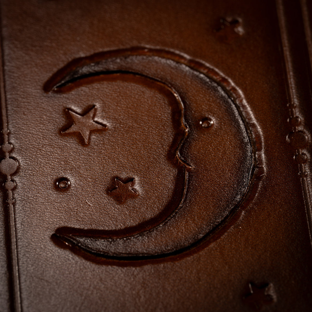Close view of the crescent moon with a face and small stars on The Astro leather tarot mat