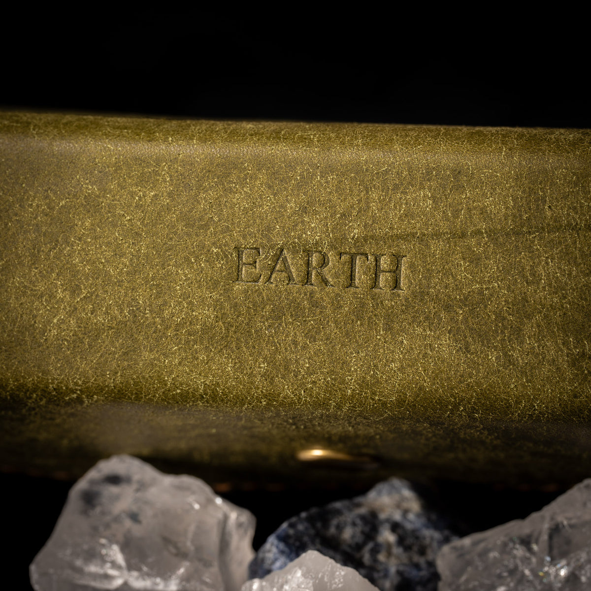 Close up of EARTH embossed into olive Pueblo leather with raw quartz in the foreground