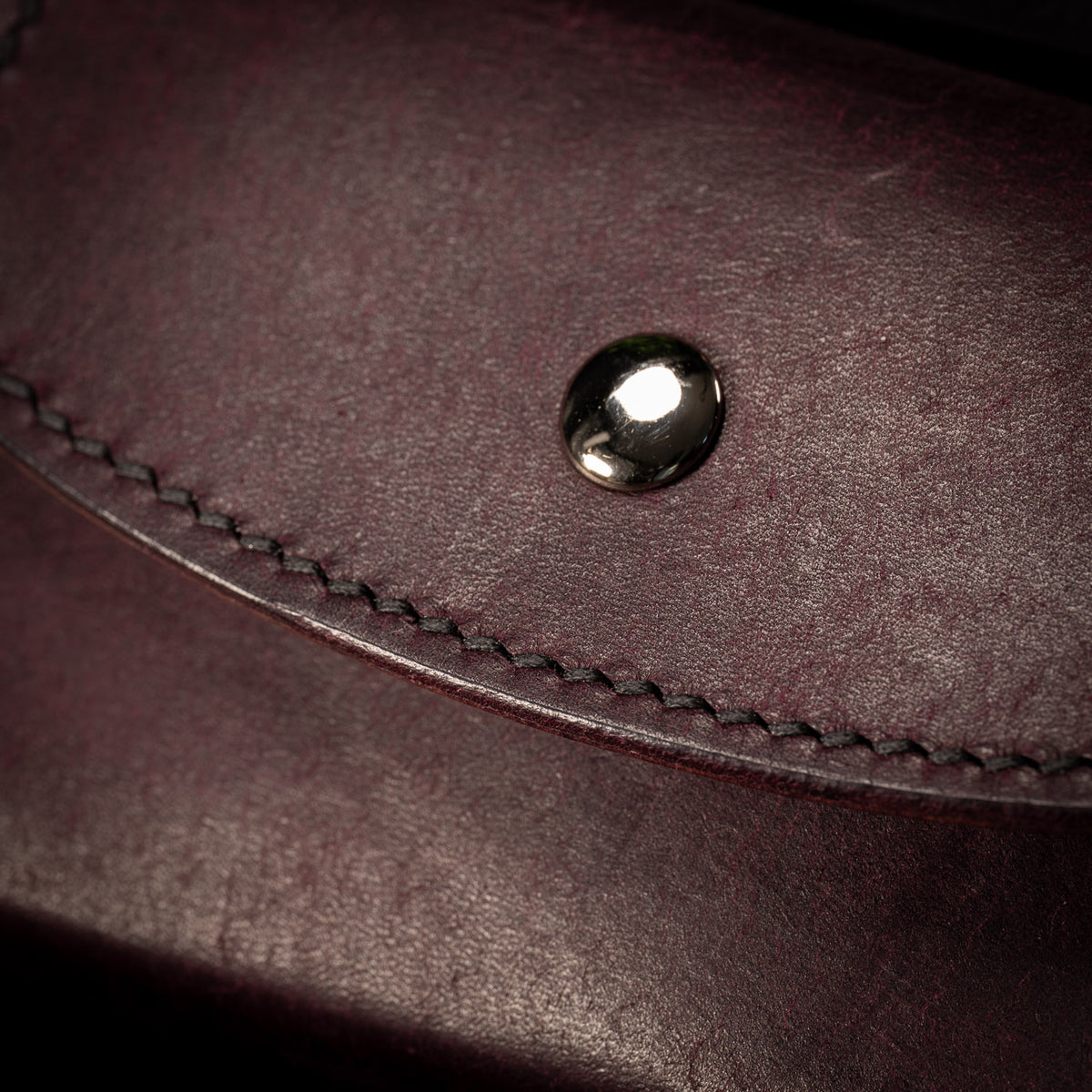 Close up of the curved flap on the plum Cosmic case, showing black saddle stitching and a polished silver stud