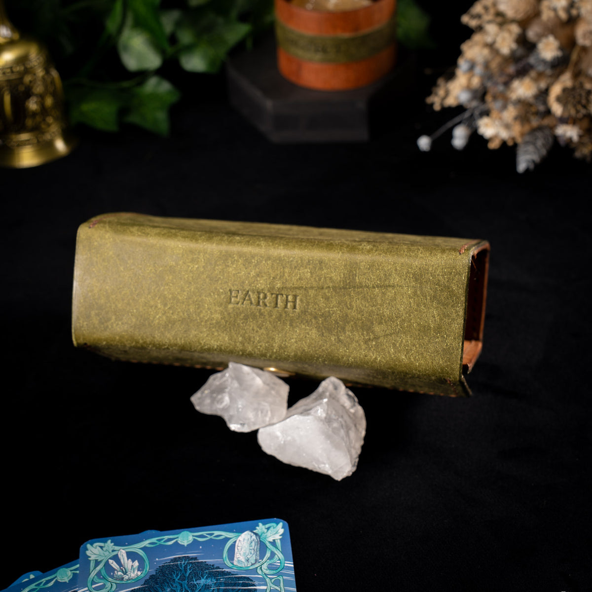 The olive Earth Oracle case seen end on with EARTH embossed across the face, resting beside two raw clear quartz points