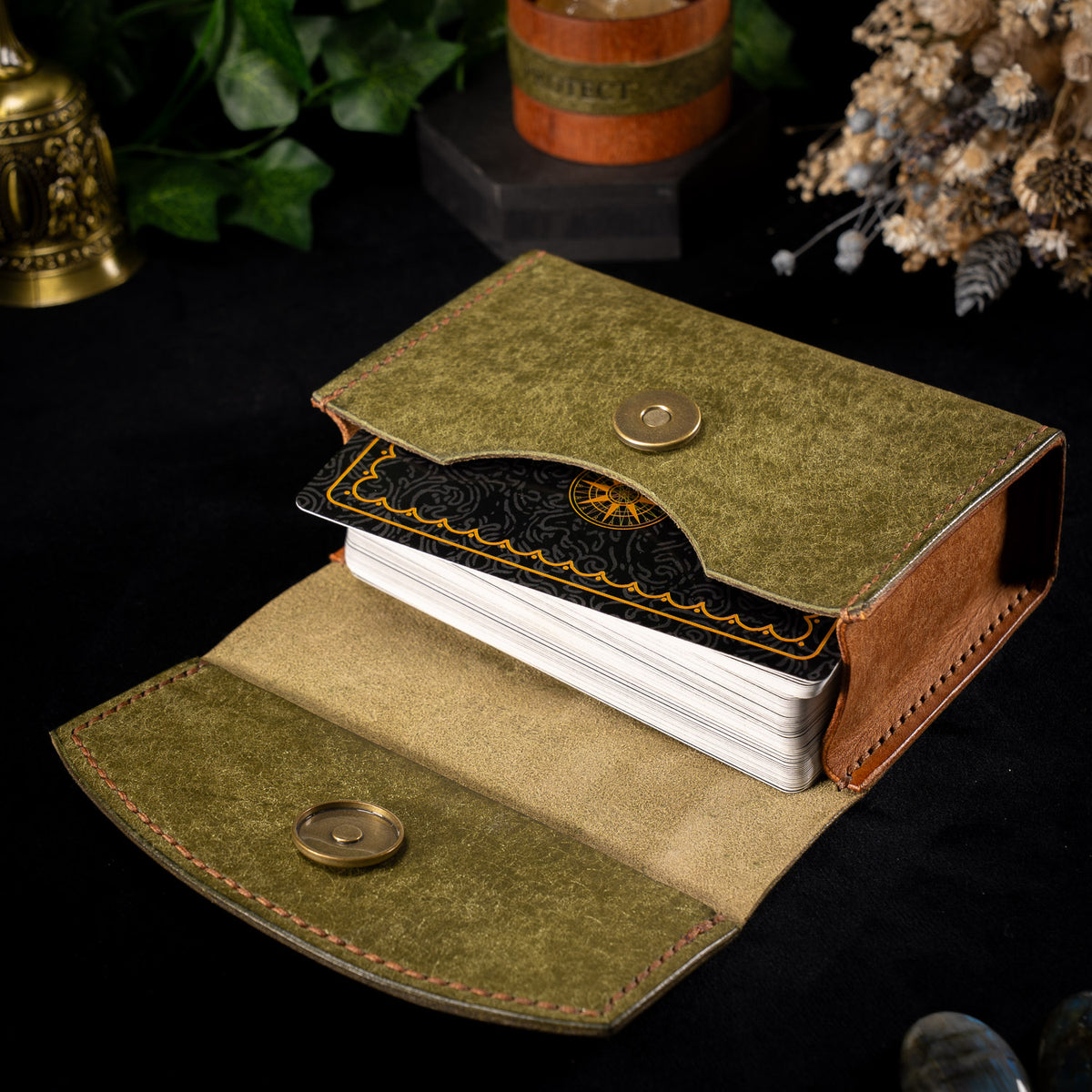 The olive Earth Oracle case open flat, brass magnetic snaps on both flap and body, holding a black and gold backed tarot deck