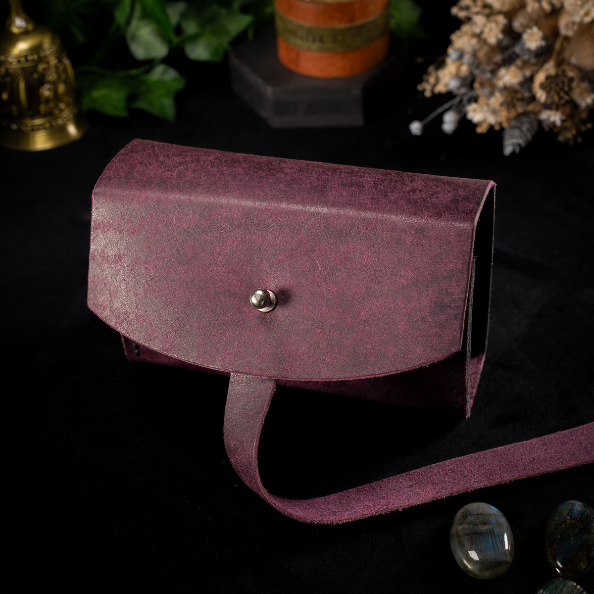 The Shroud in Prugna, the Cosmic colourway, closed with the wrap strap hanging loose, shown at an angle beside polished labradorite stones