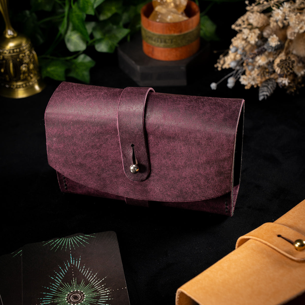 The Shroud in Prugna, the Cosmic colourway, with the strap wrapped and fastened, tarot cards in the foreground and the Bone Air version behind