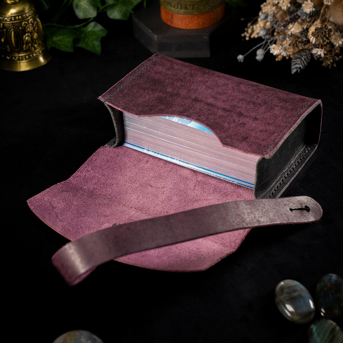 The Shroud in Prugna, the Cosmic colourway, open flat with its wrap strap unfastened alongside, showing the suede lined interior and a tarot deck resting inside